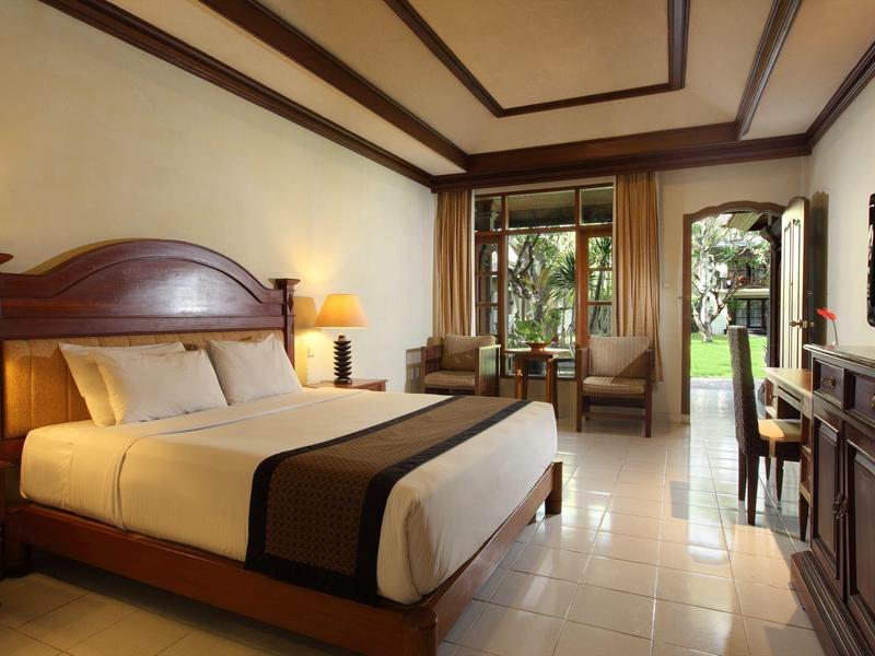 Gezellige hotelkamer met tweepersoonsbed, bank, tv en toegang tot terras met uitzicht op tuin.