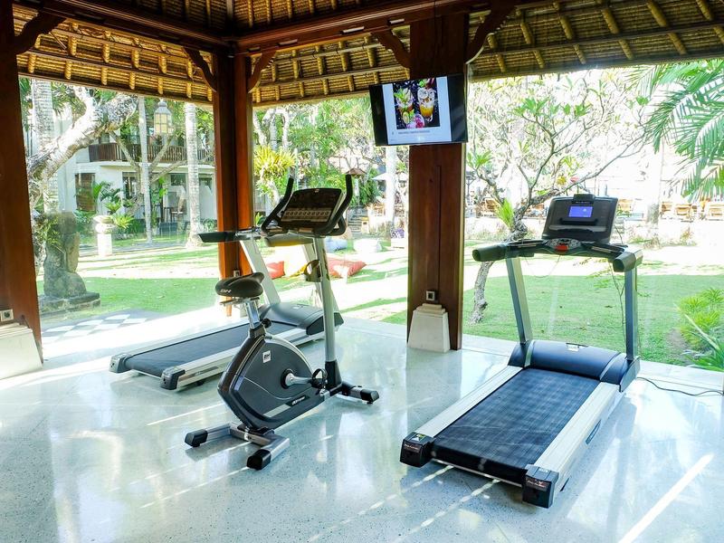 Lichte fitnessruimte met loopband en hometrainer met uitzicht op een tuin.