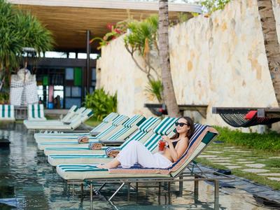Mujer relajándose en una tumbona junto a la piscina del hotel con palmeras y hamaca al fondo.