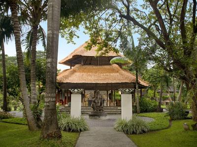 Entrada a un pabellón con techo de paja rodeado de árboles y césped verde en un resort tropical
