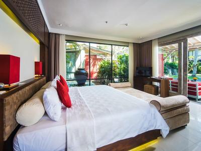 Habitación de hotel moderna con cama grande, decoración roja, luz natural y vista al jardín.