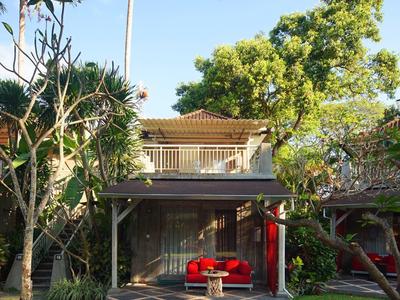 Jardín de hotel moderno con pabellón, sofá rojo y árboles tropicales bajo cielo despejado.