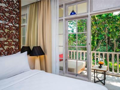 Acogedora habitación de hotel con cama grande y balcón con vista a jardín verde.