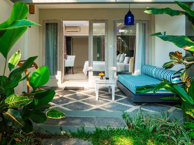 Vista de una terraza con sofá y mesa, rodeada de plantas verdes, frente a una habitación de hotel.