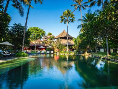 Piscina tranquila rodeada de palmeras y tumbonas frente a un resort tropical bajo el sol.