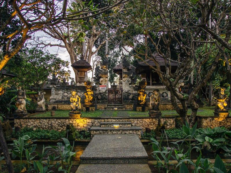 Un jardín con un camino de piedra y estatuas doradas, rodeado de árboles y plantas en un área de templo.