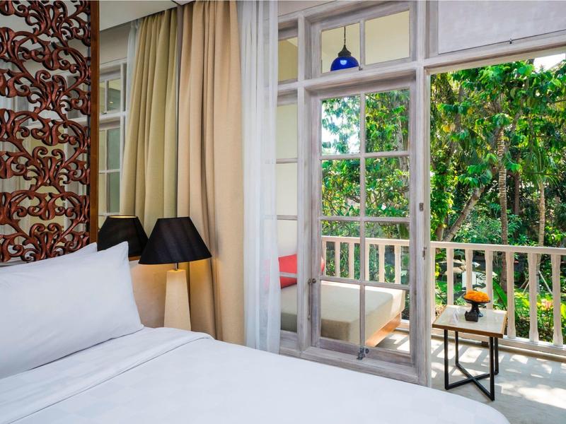 Acogedora habitación de hotel con cama grande y balcón con vista a jardín verde.