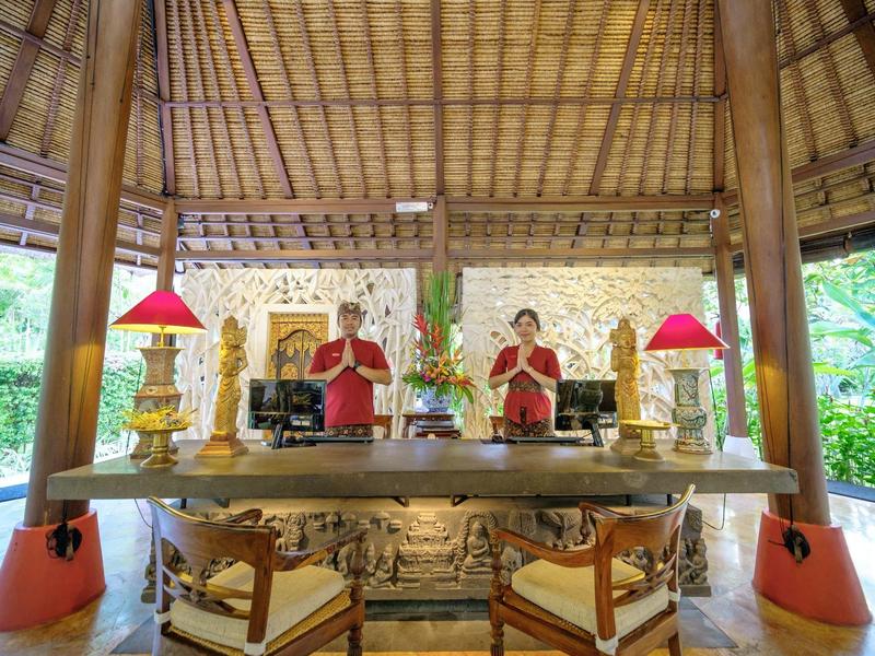 Recepción abierta de hotel con interior tradicional de madera y dos empleados con ropa roja.