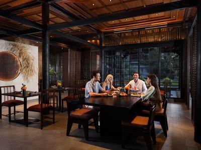 Vier personen zitten aan een houten tafel in een modern restaurant met grote ramen.