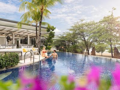 Zwei Personen sitzen am Pool eines Hotels mit Palmen und ruhiger Umgebung.