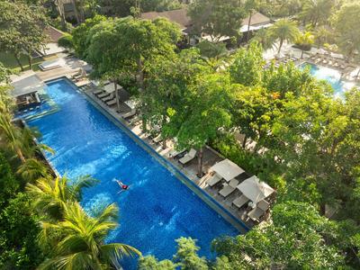 Überblick über einen rechteckigen Pool in einem von Bäumen umgebenen Hotelgarten mit Liegestühlen.