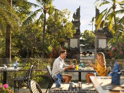 Paar sitzt an einem Tisch im Freien in einem tropischen Garten mit Tempelturm im Hintergrund.