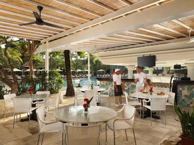 Open restaurant met witte tafels en stoelen onder houten overkapping naast een zwembad.