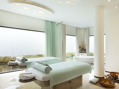 Heller Wellnessraum mit zwei Massageliegen, großem Fenster und gemütlicher Atmosphäre.