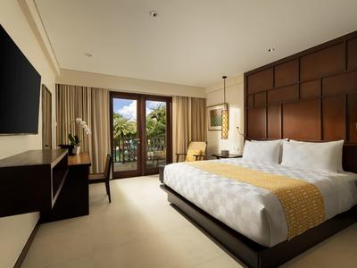 Elegante hotelkamer met groot bed, bureau en balkon met uitzicht op groen.