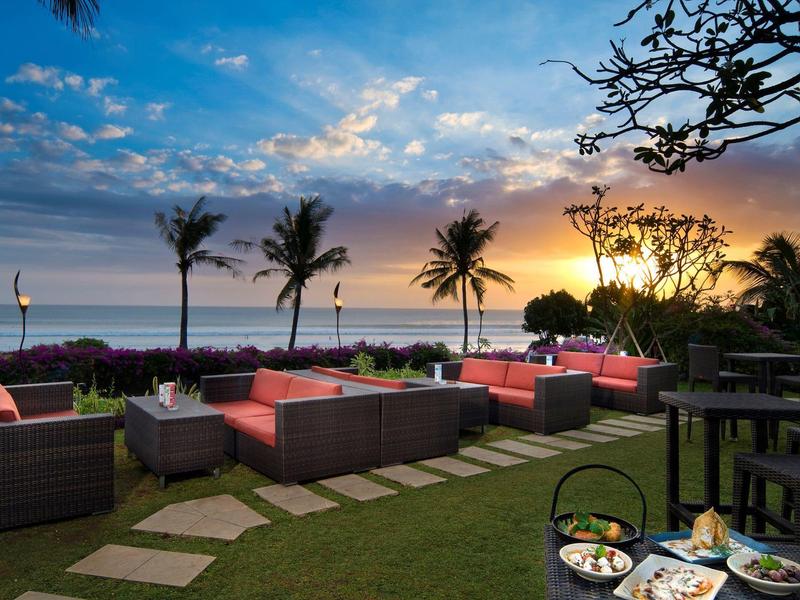 Loungegedeelte met zitmeubels, planten en uitzicht op zonsondergang over de zee.