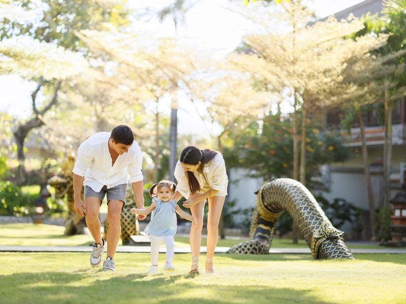 Ouders rennen met hun peuter op het gras in een hoteltuin.