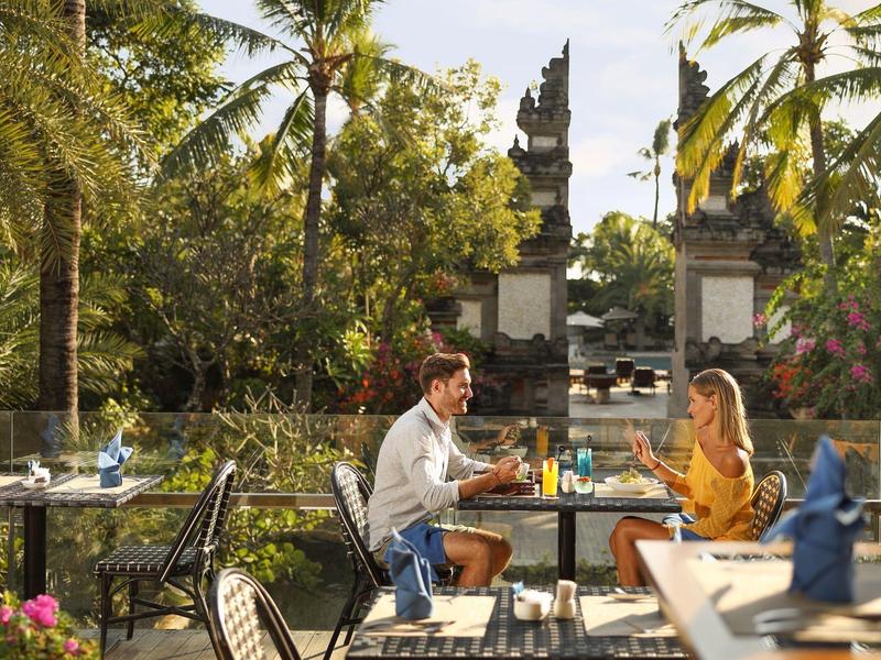 Koppel geniet van ontbijt in de tropische tuin van een hotel met weelderig groen en traditionele poortbogen.