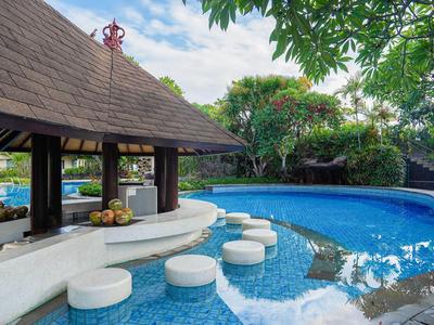 Poolbar mit runden Sitzgelegenheiten im Wasser, umgeben von tropischem Grün und blauem Himmel.