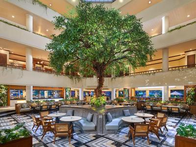 Heller Hotel-Lobbybereich mit Innenbaum und elegant angeordneten Tischen und Stühlen