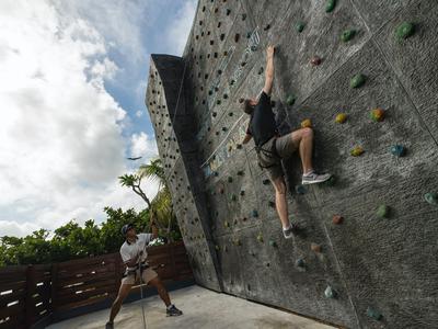 Person klettert an Kletterwand im Freien, eine andere Person sichert am Boden.