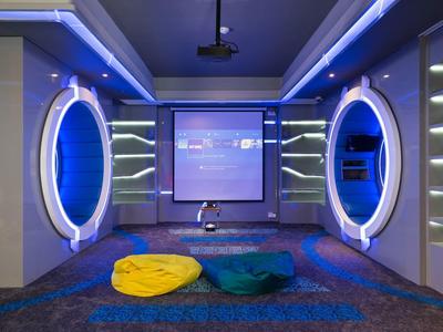 Salle de cinéma moderne avec grand écran, cercles lumineux bleus et poufs colorés au sol.