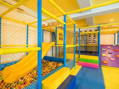 Aire de jeux intérieure colorée avec mur d'escalade, toboggan et piscine à balles dans une salle de jeu d'hôtel.