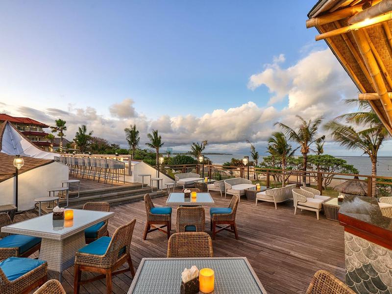 Terrasse d'hôtel ensoleillée avec sièges et vue sur la mer par ciel clair.
