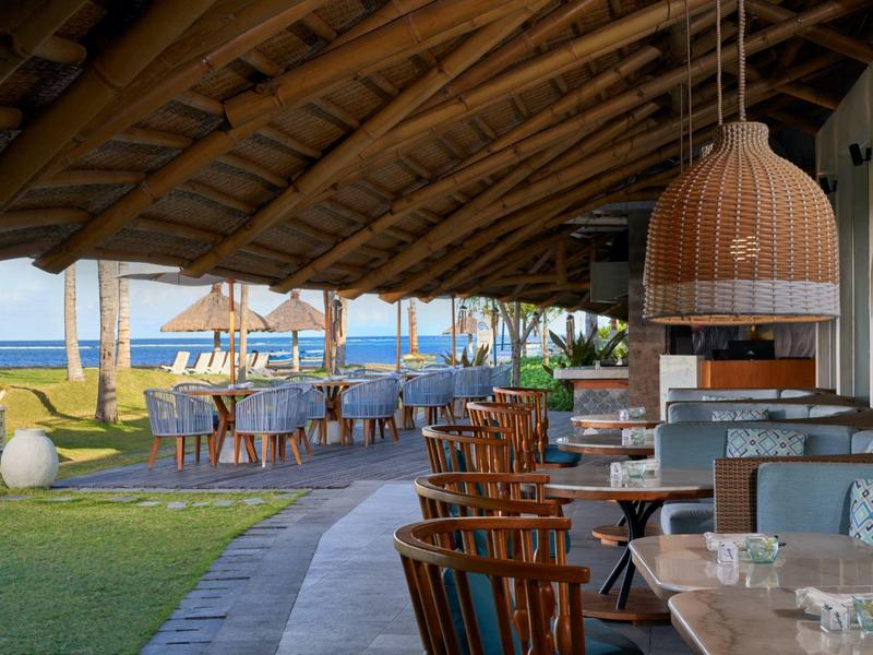 Salon extérieur couvert et espace repas avec vue sur la mer par une journée ensoleillée