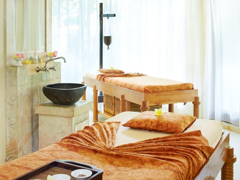 Deux tables de massage luxueuses avec couvertures brunes dans une pièce de spa lumineuse avec des rideaux.