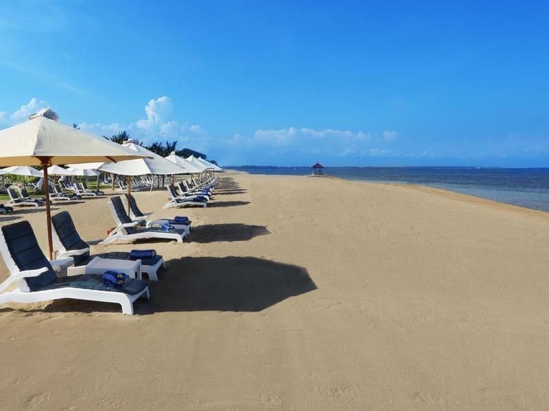 Plage de sable vide avec chaises longues et parasols sous un ciel bleu au bord de la mer.