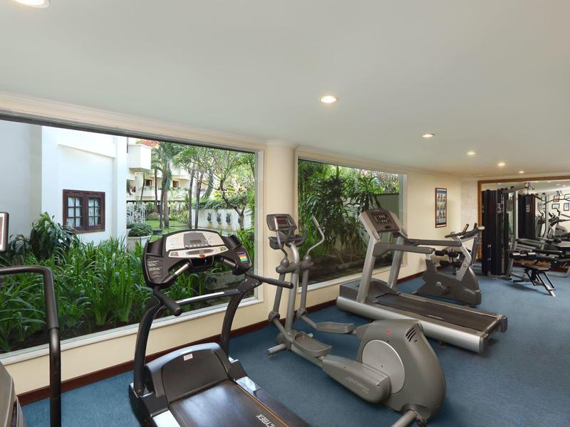 Salle de sport avec tapis de course modernes et vélos elliptiques devant de grandes fenêtres donnant sur la verdure.