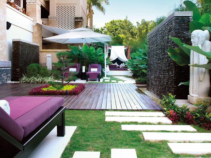 Modern hotel outdoor area with garden, wooden deck, greenery, and lounge chairs.