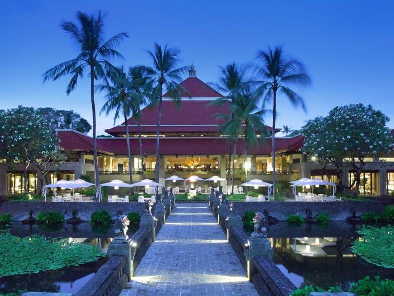 Luxury hotel with illuminated pool and palm trees at dusk