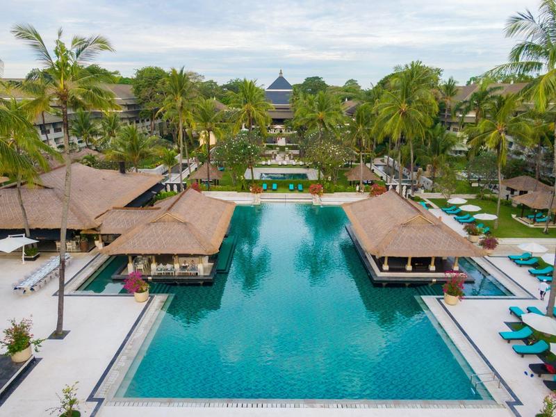 Large pool with pool bars and palm trees in tropical resort during daylight