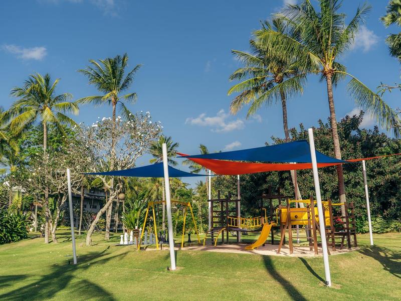 Playground with climbing frame and sunshades in tropical garden with palm trees.