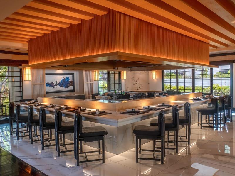 Modern hotel bar area with a central illuminated bar and black chairs.