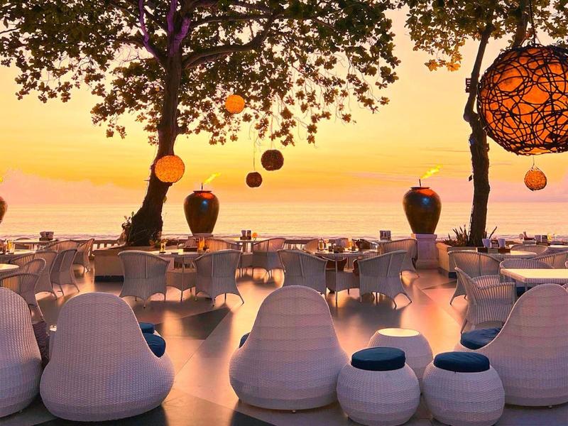 Evening beach terrace with bean bags and lanterns at sunset.