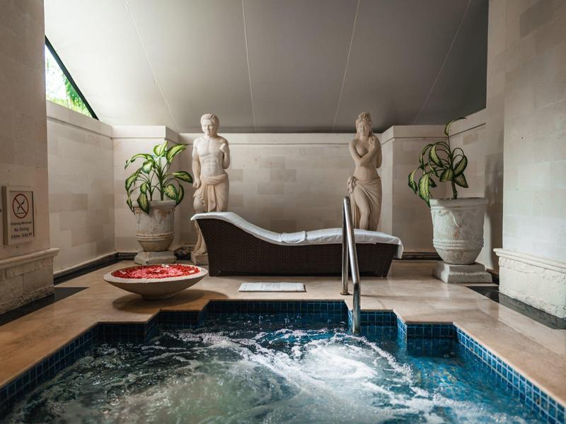 Modern wellness area with whirlpool, lounge chair, and sculptures in an elegant setting.