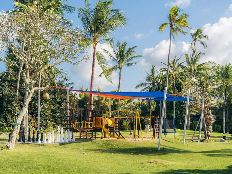 Children's playground with climbing frame and swings on green lawn with palm trees behind