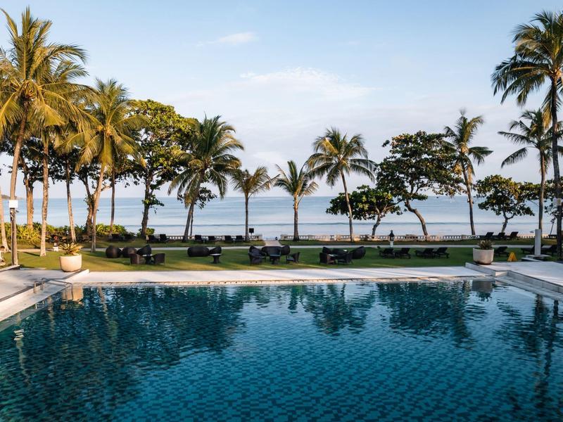 A pool in a tropical resort with palm trees and a view of the sea.