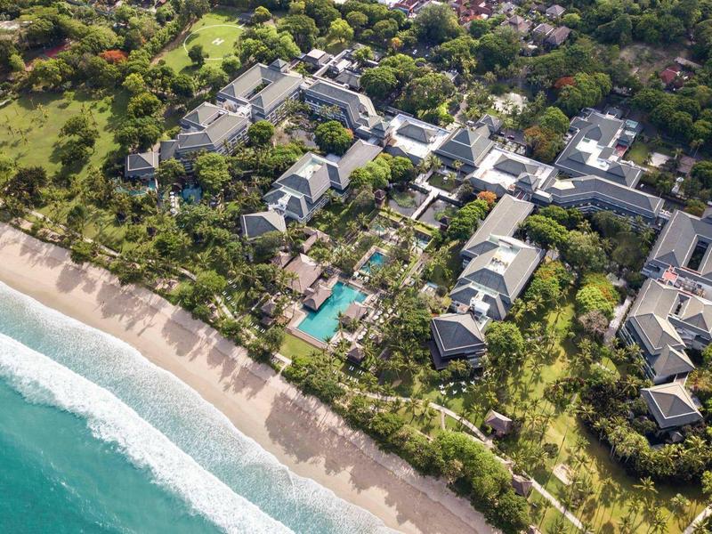 Aerial view of a resort with pool, green garden, and beach by turquoise sea.