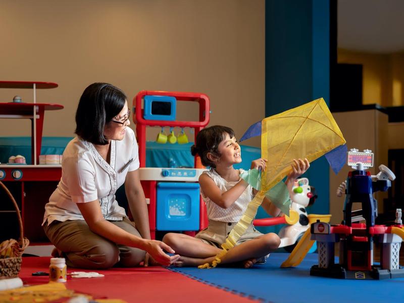 Two children playing with toys on colorful carpet in bright indoor space.