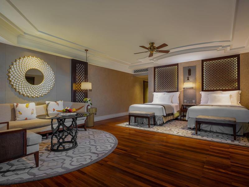 Elegant hotel room with two double beds, cozy seating area, and modern wooden flooring.