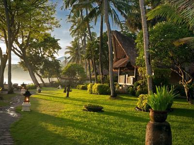 Grüner Garten mit Palmen, traditionellen Hütten und Sonnenlicht am Seeufer.