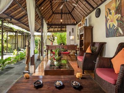 Überdachte Lounge mit Holzmöbeln, Kissen und tropischer Gartenaussicht in einem Hotel.