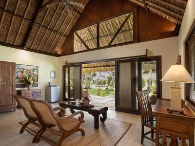 Innenraum eines gemütlichen Zimmers mit Holzdecke, zwei Sesseln, Schreibtisch und großen Glastüren zum Garten.