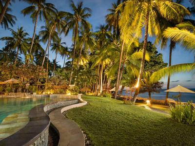 Abendaufnahme eines tropischen Resorts mit Pool, Palmen und Blick aufs Meer.