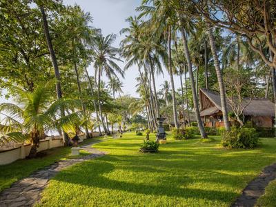 Grüner Garten mit Palmen und Bungalows am sonnigen Strand