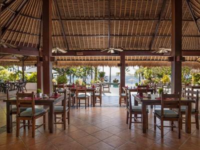 Offener Restaurantbereich mit Holzdach, mehreren Tischen, Stühlen und Blick auf tropische Außenanlage.